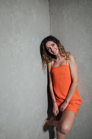 a woman in an orange dress stands on one leg in a roomの写真素材