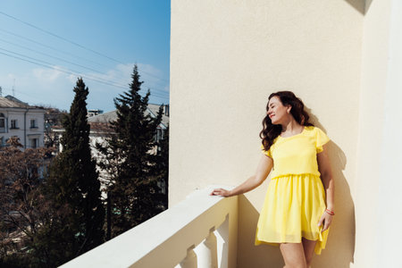 beautiful brunette woman in a yellow dress stands on the balcony of the buildingの写真素材