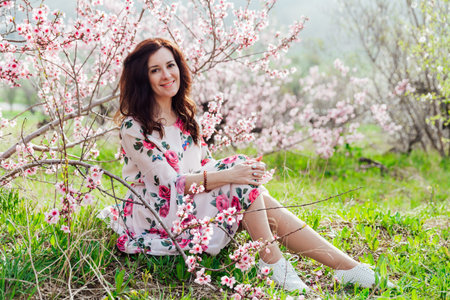 woman sitting in a garden of blooming pink trees nature park springの写真素材