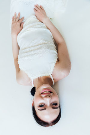 beautiful brunette woman in a white dress lies in a bright roomの写真素材