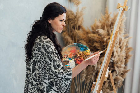 female artist draws with a brush using a palette on an easel in an art studio teacherの写真素材