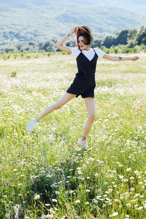 a cheerful woman jumps in a green field with daisies on a walkの写真素材