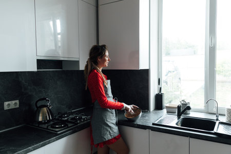 a woman cook in an apron prepares food and looks out the windowの写真素材