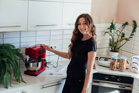 a woman in the kitchen shows a kitchen mixer for making cakesの写真素材