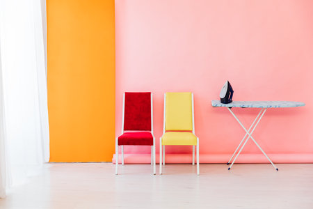 ironing board with iron on pink background yellow red chairの写真素材