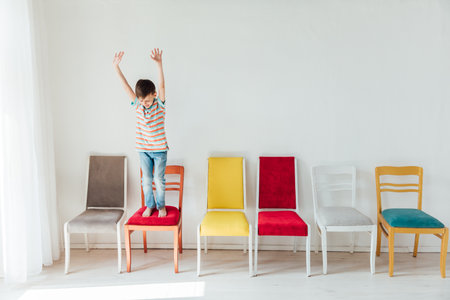 Cheerful little boy and many different colored chairsの写真素材