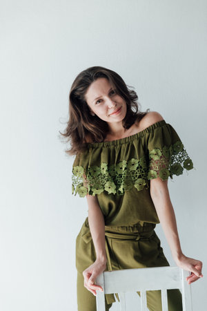 Beautiful brunette woman in green clothes posing in bright roomの写真素材