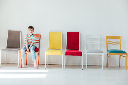 Cheerful little boy and many different colored chairsの写真素材