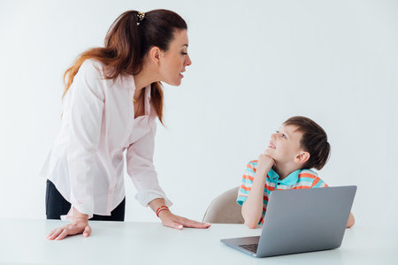 Woman with boy watching online laptop at table at schoolの写真素材