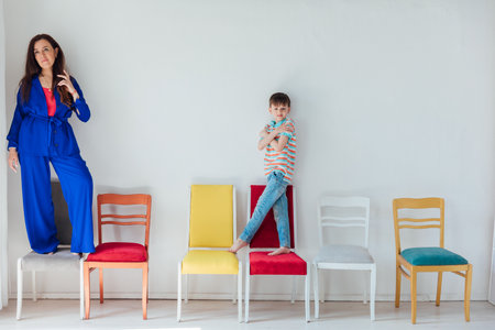 Boy and woman sitting on different chairs in white room interiorの写真素材