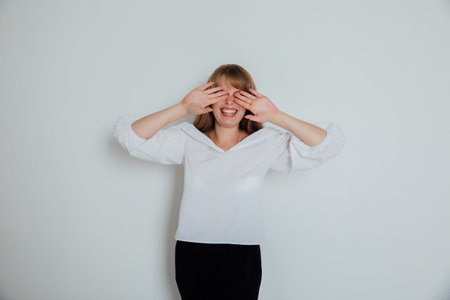 A woman closes her eyes with her hands against a light background in the roomの写真素材