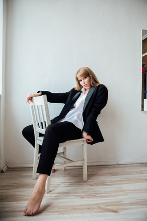 Beautiful young fashionable woman in black business suit sitting on a chairの写真素材