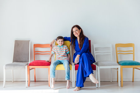 Boy and woman sitting on different chairs in white room interiorの写真素材