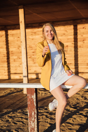 a blonde girl in a yellow jacket sits on a wooden benchの写真素材