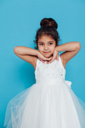 a little girl in a white dress with a hairstyle poses on a blue backgroundの写真素材