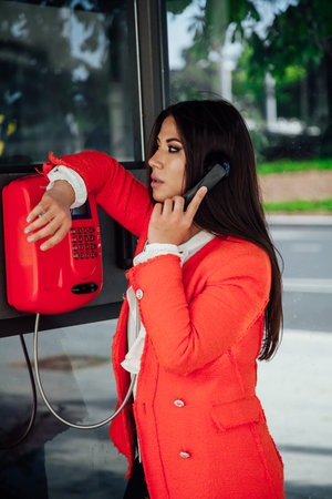 a brunette woman talking on the phone in a booth on the streetの写真素材