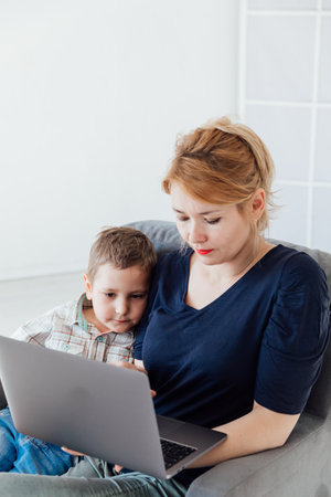 Beautiful woman with son online on computer at homeの写真素材
