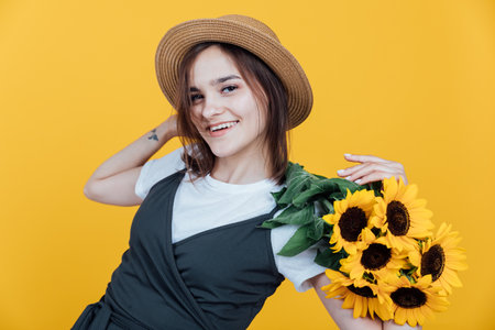 Woman in a hat with a bouquet of daisies on a yellow backgroundの写真素材