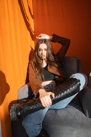 Woman wearing sunglasses posing sitting on orange background at sunsetの写真素材