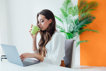 beautiful brunette with a cup at a laptop communication online remote workの写真素材