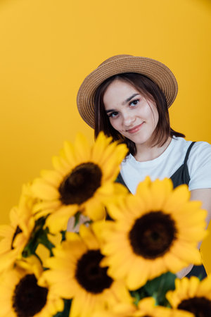 Portrait of a beautiful young woman with sunflower flowers on a yellow backgroundの写真素材