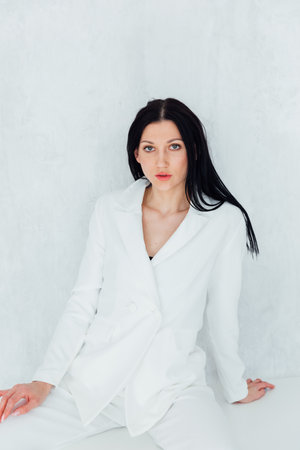 Fashionable brunette woman in white suit sitting on tableの写真素材