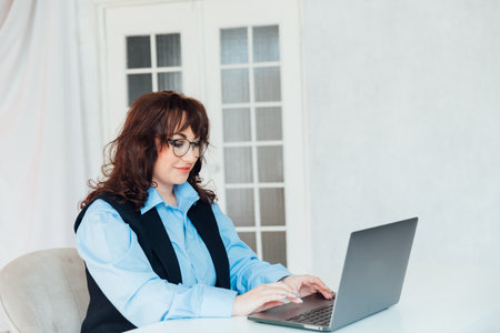 Portrait of Young Successful Caucasian Businesswoman Sitting at Desk Working on Laptop Computer in City Office.の写真素材