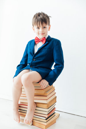 Boy in jacket sitting on a stack of booksの写真素材