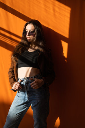 Woman wearing sunglasses posing on orange background at sunsetの写真素材
