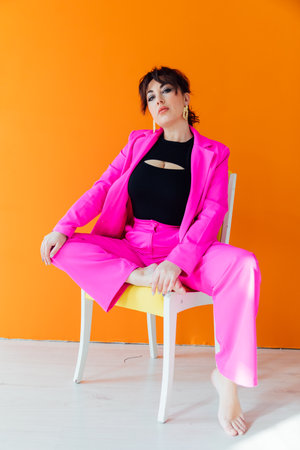 Woman in suit posing on a chair on an orange backgroundの写真素材