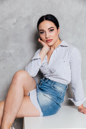 Beautiful fashionable woman in denim skirt posing in studio on gray backgroundの写真素材