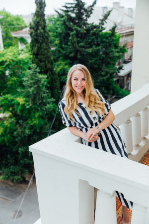 Beautiful woman in summer striped dress on outdoor balcony smilingの写真素材