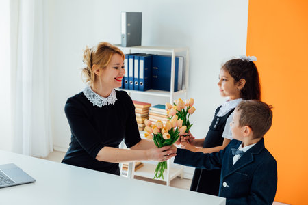 boy and a girl give flowers to a teacher for a holidayの写真素材