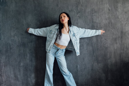 Beautiful young brunette woman in jeans and a jacket posing on a gray backgroundの写真素材