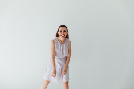 brunette woman in light summer dress smiling at white wallの写真素材