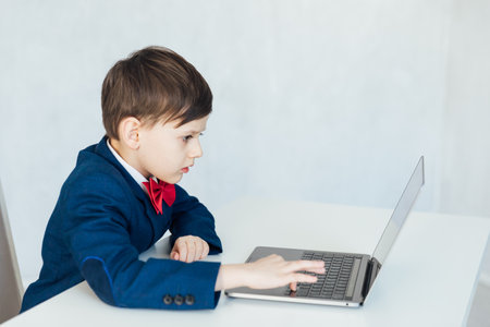 Schoolboy In Jacket At Desk Playing In Laptopの写真素材