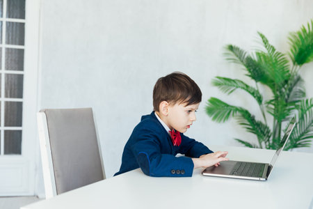 Schoolboy In Jacket At Desk Playing In Laptop