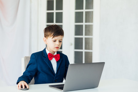 Little boy in business suit studying playing on laptop onlineの写真素材