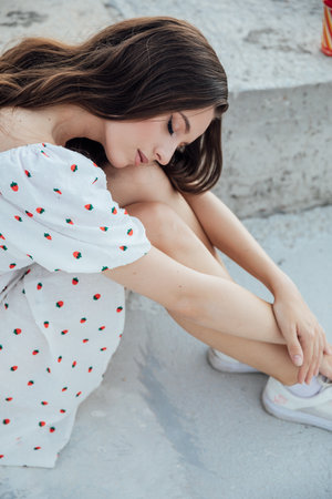 Beautiful brunette woman in summer dress sitting on stone floor and smilingの写真素材