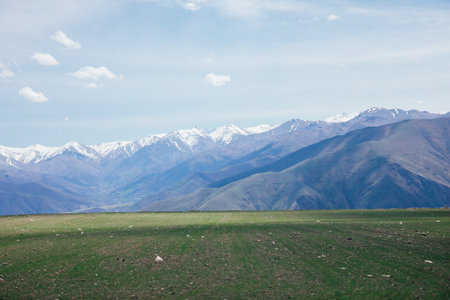 A beautiful landscape of snow-capped mountains and green meadows and a sky with cloudsの写真素材