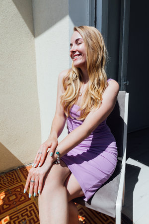 Beautiful fashion blonde woman sitting on a chair in purple summer dressの写真素材