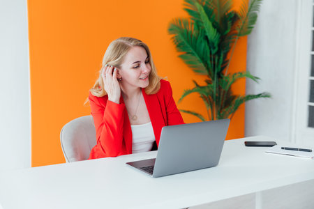 Business woman in red suit at desk with laptop in office training onlineの写真素材