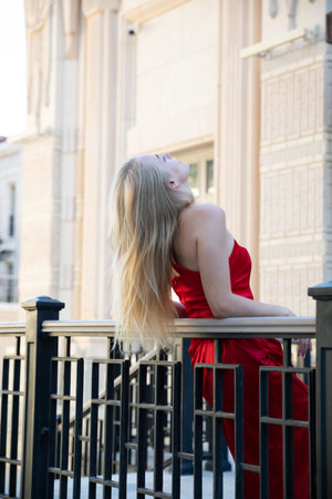 Beautiful fashion blonde woman in red dress standing on balconyの写真素材