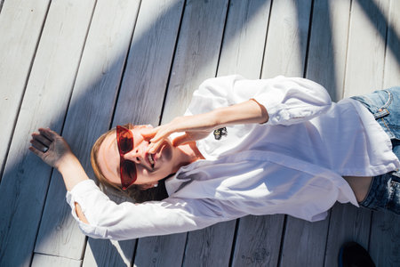 Beautiful woman in sunglasses lying on wooden floorの写真素材