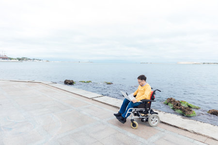 A man in a wheelchair came to the sea to work online on a laptop for businessの写真素材