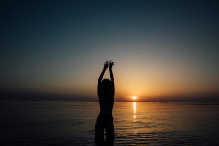 Silhouette of slender woman on the beach at sunset by the seaの写真素材