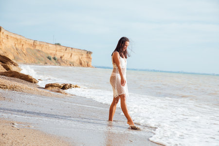 Brunette in a light dress walking on a sandy sea beachの写真素材