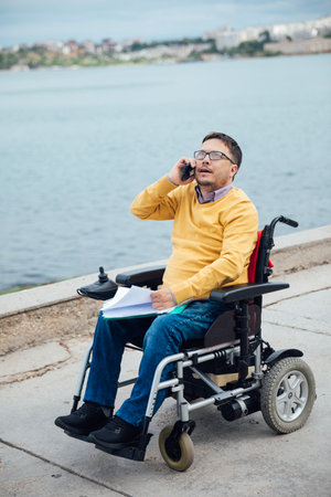 Man in wheelchair working on laptop while making a callの写真素材