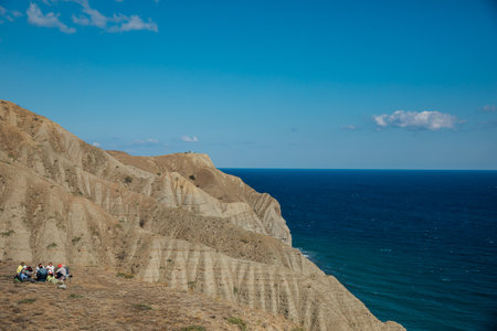 People tourists relaxing hiking on top of a cliff by the blue seaの写真素材