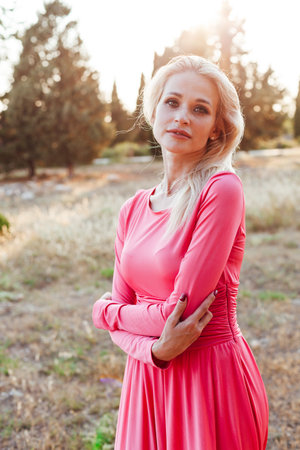 Blonde woman in pink dress at sunset in parkの写真素材